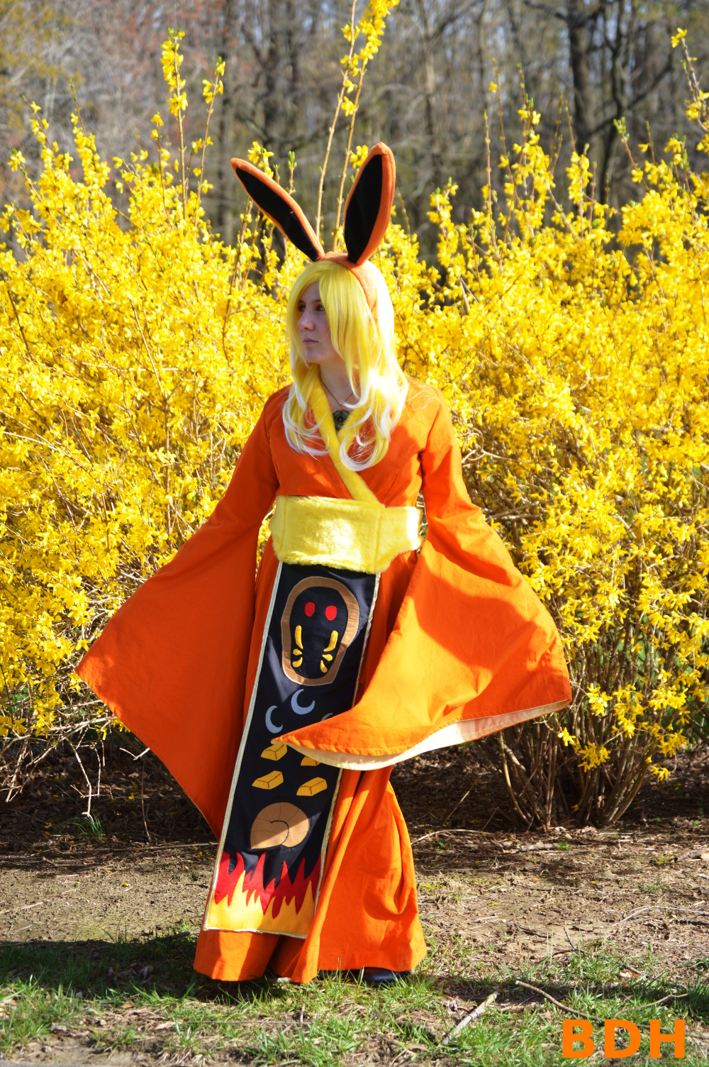 Flareon cosplay involving an orange gown with bell sleeves, long orange ears, and a banner depicting Kabuto and other TPP symbols.