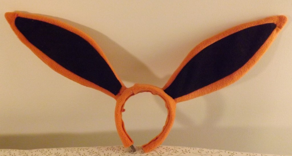 A photo of an orange headband with long orange and black ears attached.