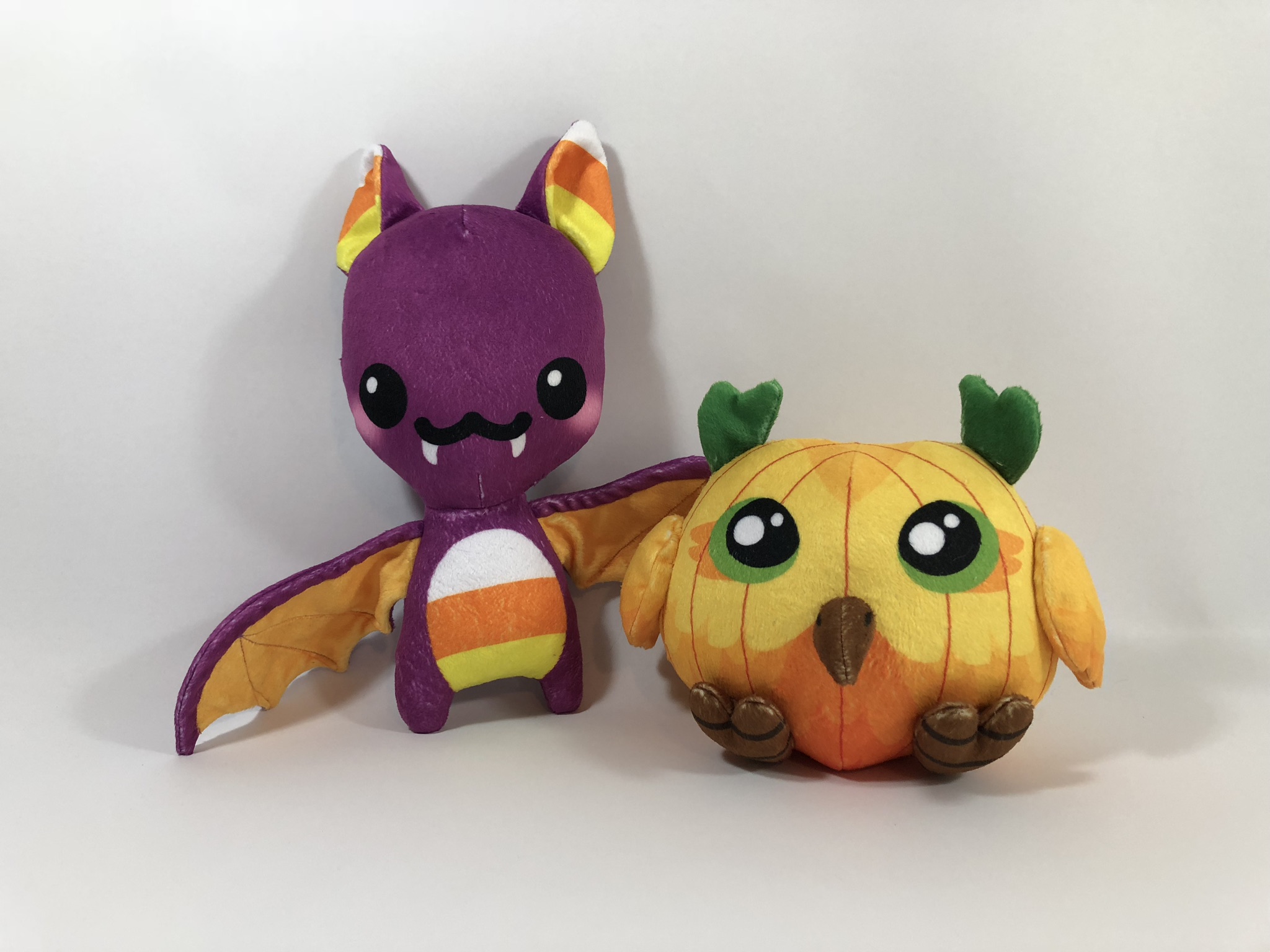 Purple and candy corn bat plush and an owl plush with a pumpkin design.