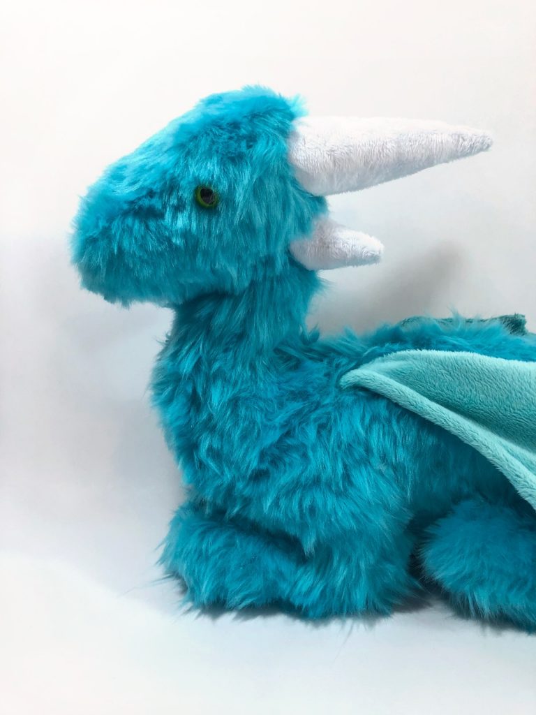 Closeup of the head and chest of the dragon plush. It has green safety eyes and white horns.