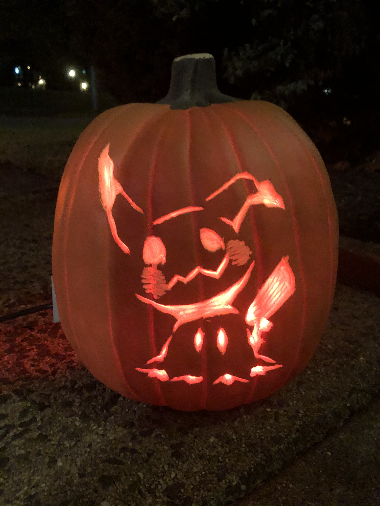 An orange foam pumpkin with Mimikyu carved on it. Mimikyu is glowing red because of a red light inside the pumpkin.