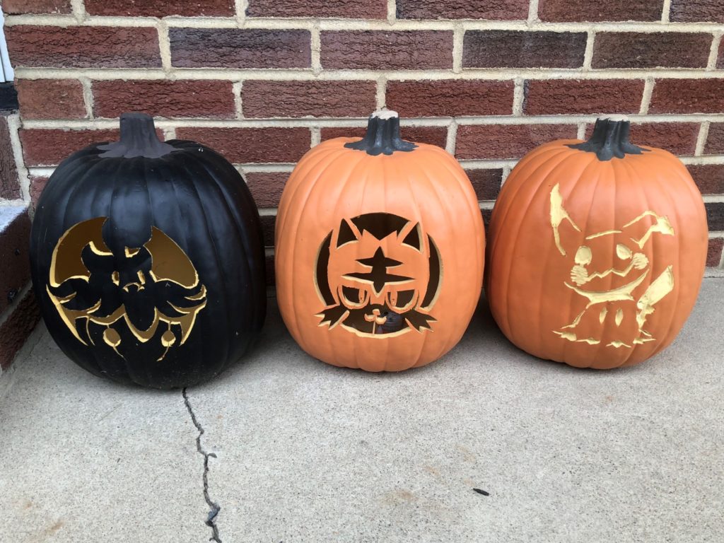 From left to right, a black foam pumpkin with Pumpkaboo carved into it, an orange foam pumpkin with Litten carved into it, and the Mimikyu foam pumpkin.