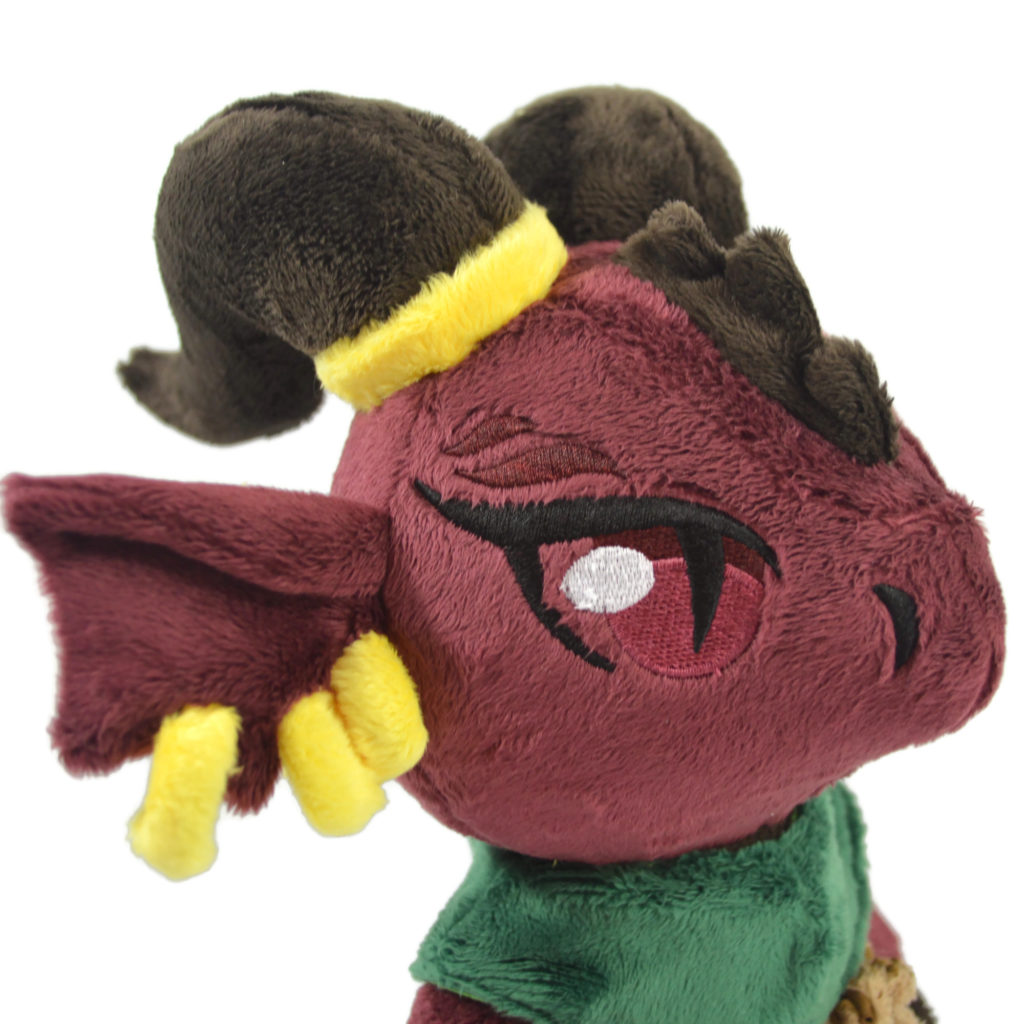 A close up photo of the red kobold's face. they have three gold earrings and a gold ring around one horn.