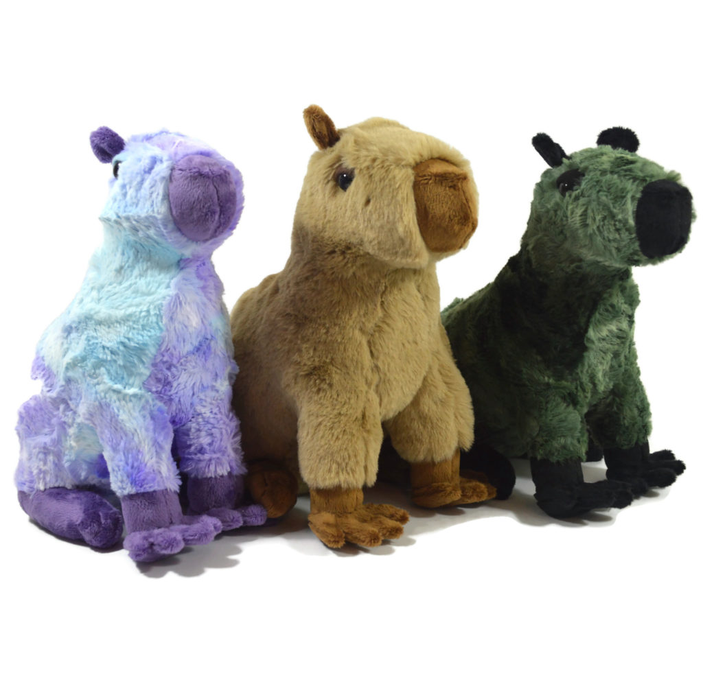 Three capybara plush in a row, with a purple and blue one on the left, a tan and brown one in the middle, and a green and black one on the right.