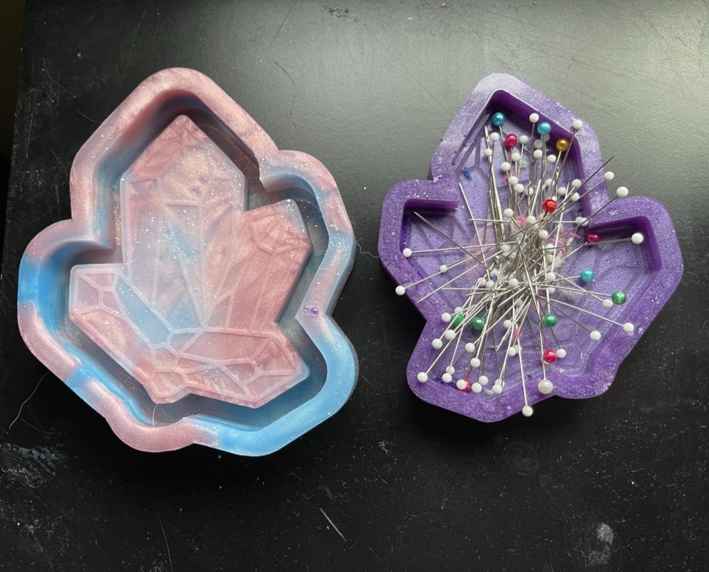 A photo of a crystal tray mold on the left and a tray made from the mold on the right. The finished tray has a magnet embedded inside it and is being used to hold sewing pins.
